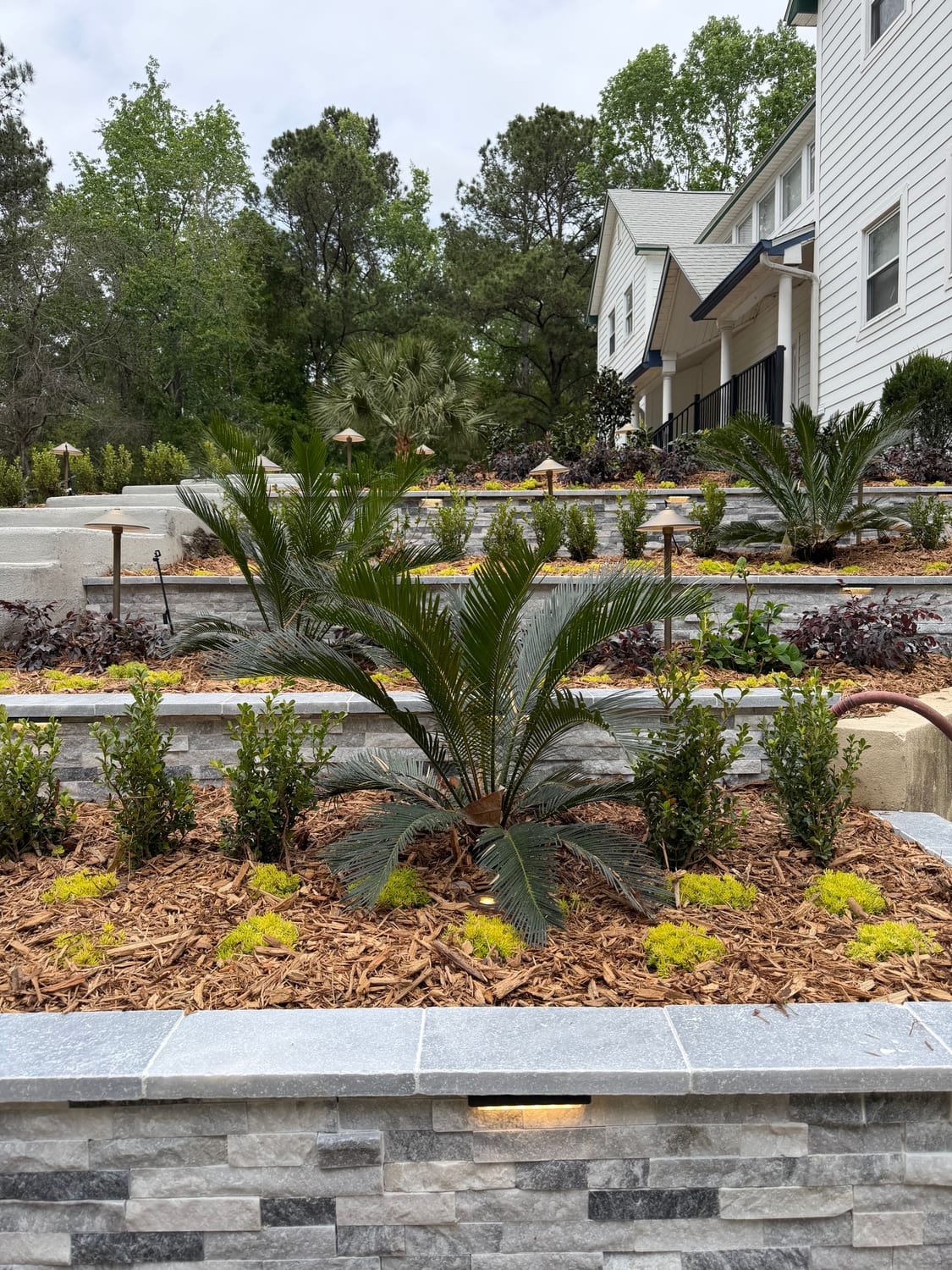 Tiered stacked-stone retaining walls with travertine caps and uplit palms