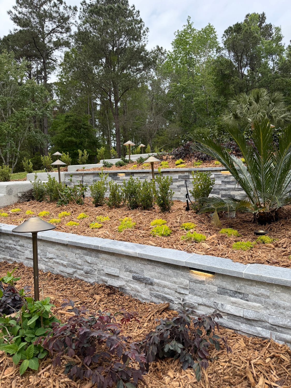 Stacked-stone retaining wall with travertine cap and path lighting