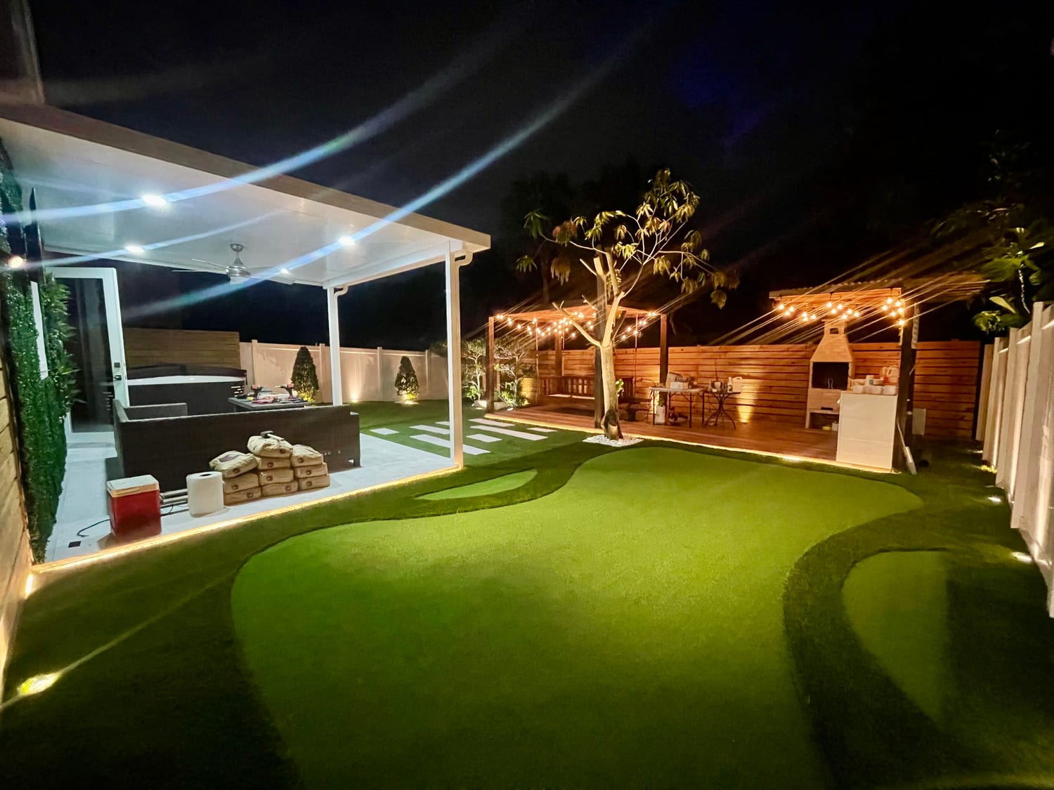 Backyard putting green with string lights and pergola at night